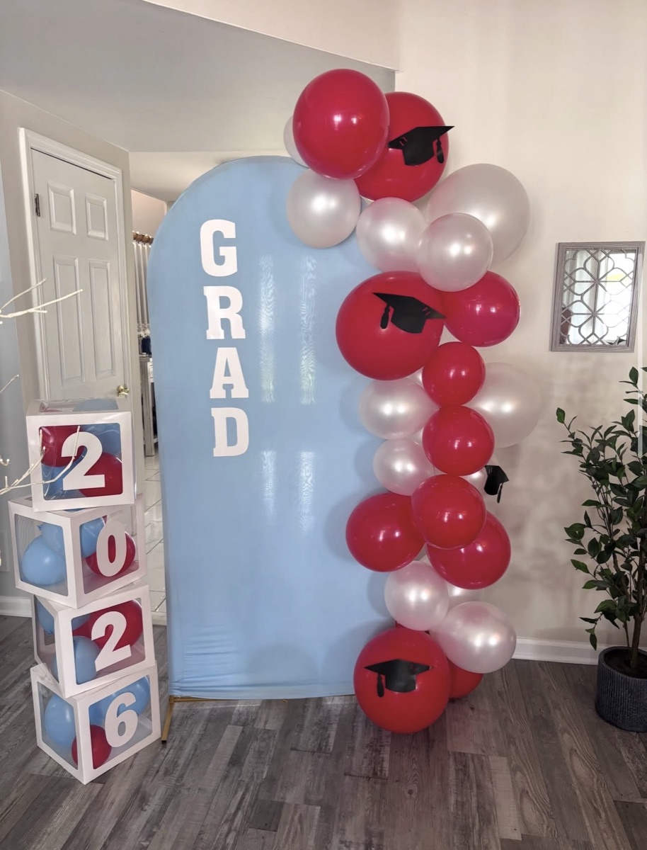 Graduation 2026 backdrop with blue arch, red and white balloon garland and graduation cap accents