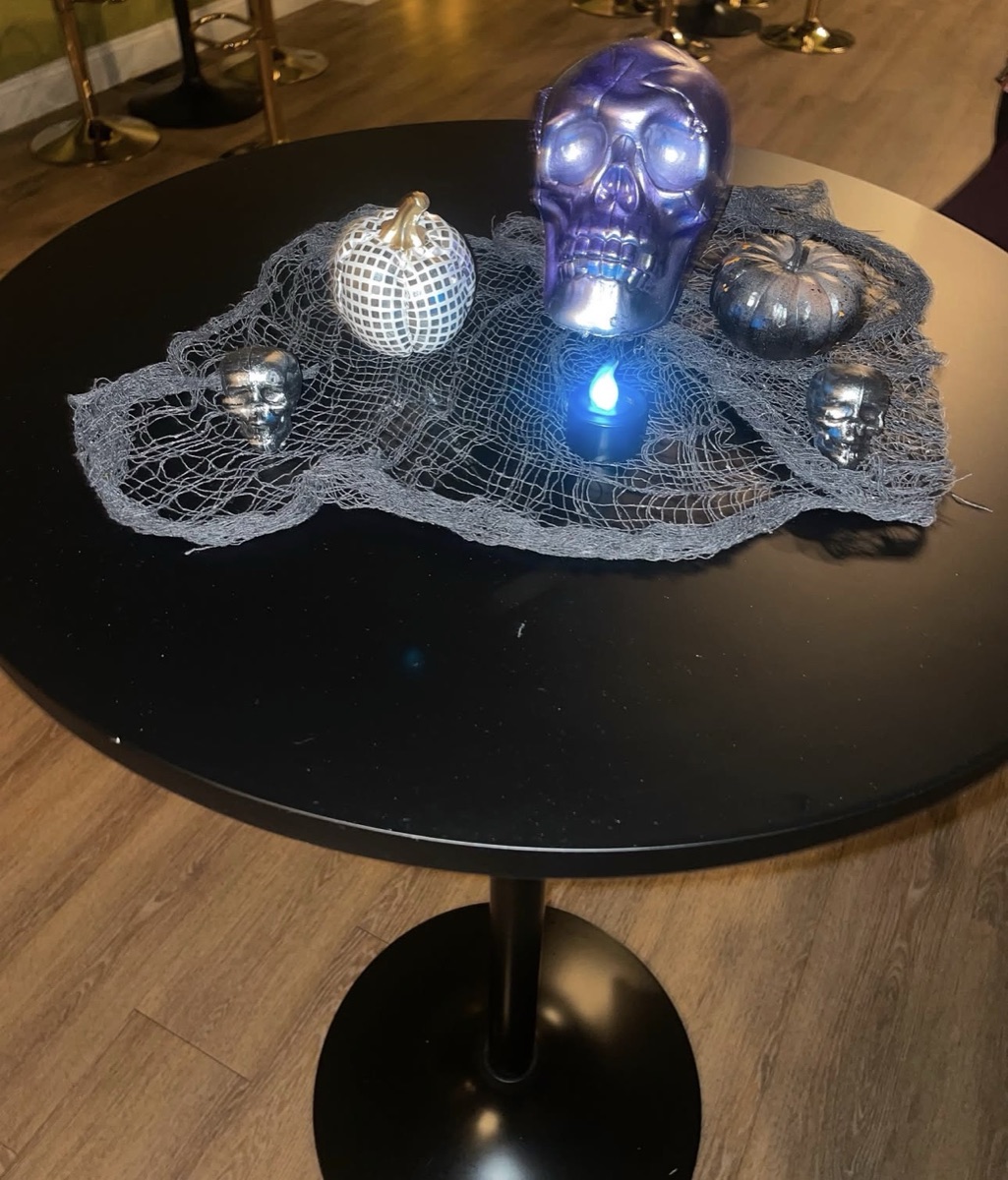 Halloween centerpiece with silver and purple skulls, pumpkins and blue candle on a black table