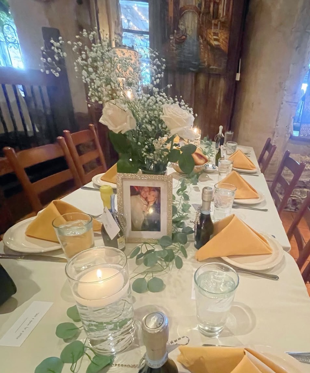 Long wedding reception table with white roses, babys breath, gold napkins and framed centerpiece